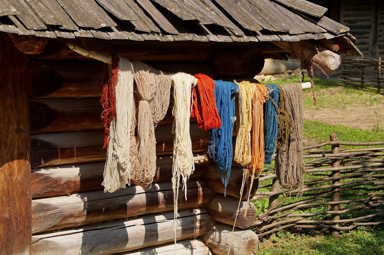 Skeins of wool dyed red, blue, yellow and cream, hung out to dry on a wooden rail