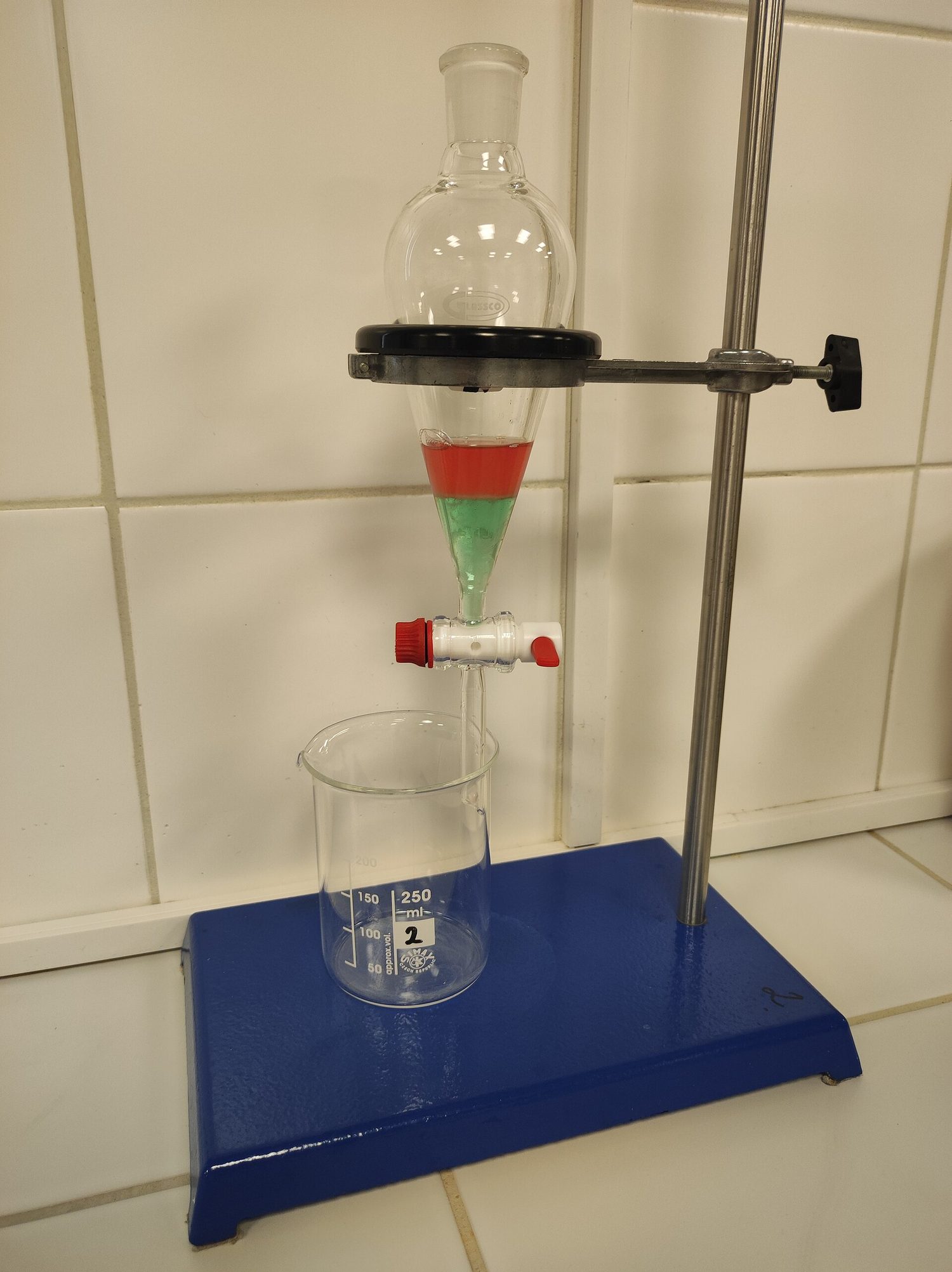 A separating funnel clamped above a beaker, holding two coloured liquid layers that do not mix