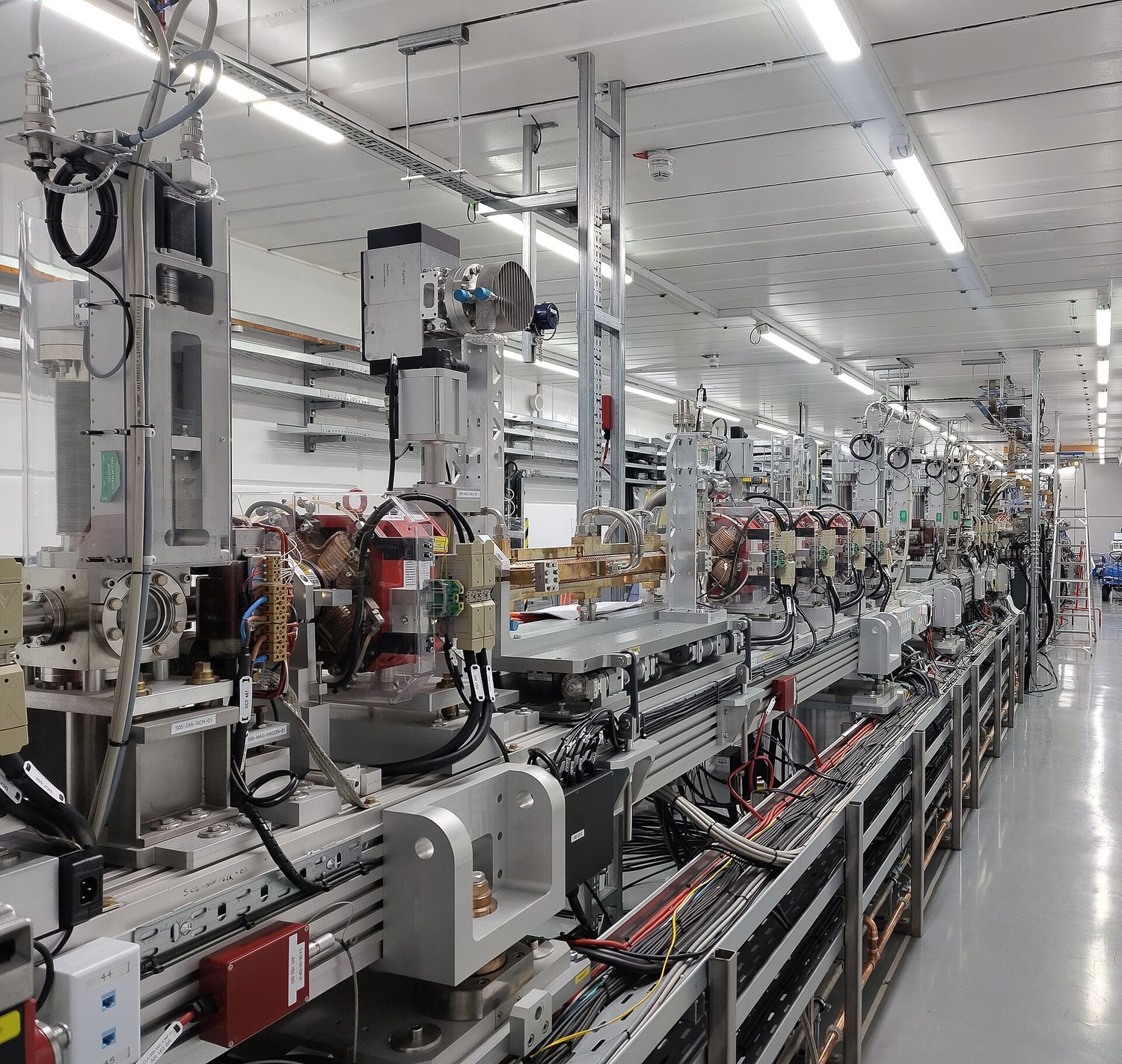 A linear accelerator hall: a long line of accelerating cavities and beam pipes running away down the room