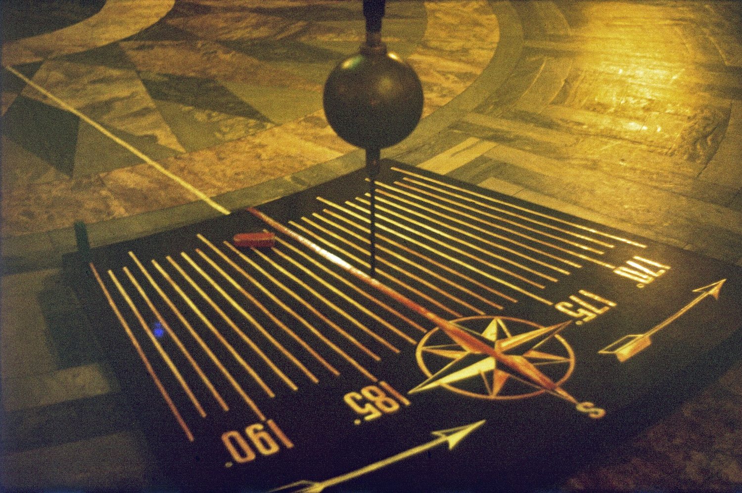 A large Foucault pendulum swinging over a marked floor