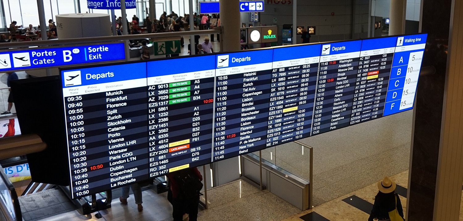 A large airport departure board listing many flight times, destinations and gates
