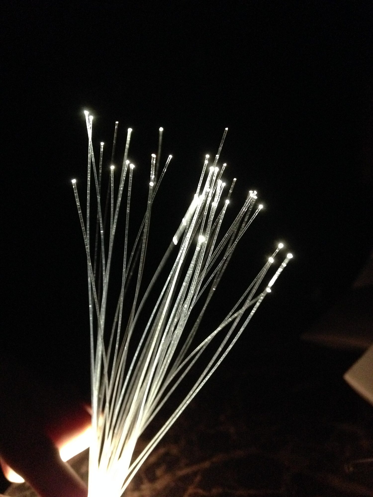 A bundle of thin glass fibres glowing brightly at their tips in a dark room