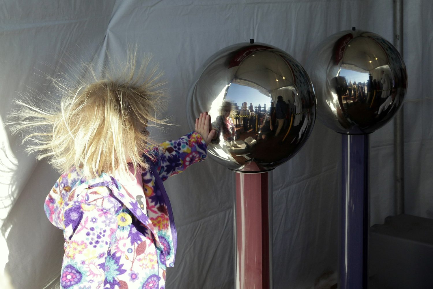 A girl touching a Van de Graaff generator dome with her hair standing straight up and pushing apart